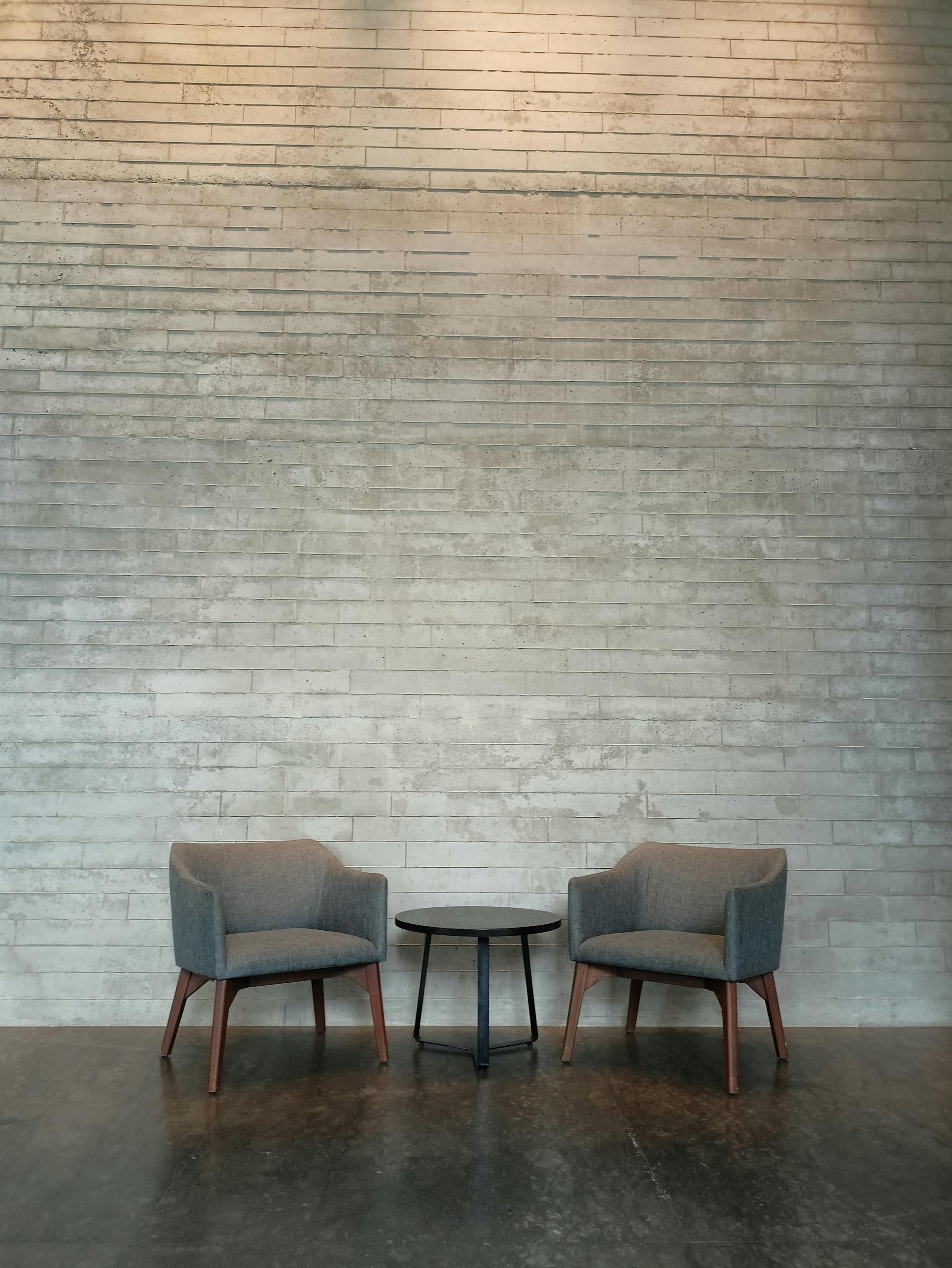 Minimalist interior design featuring two chairs and a coffee table against a brick wall in Jakarta.