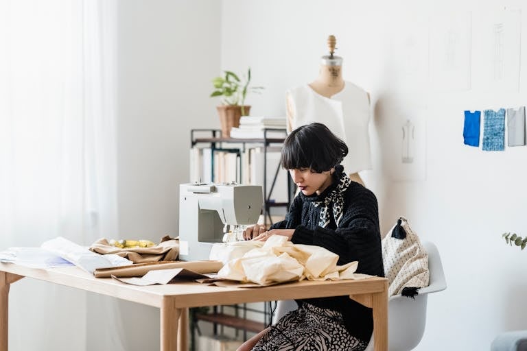 Asian seamstress focused on sewing in a bright, modern workshop with a sewing machine and mannequin.