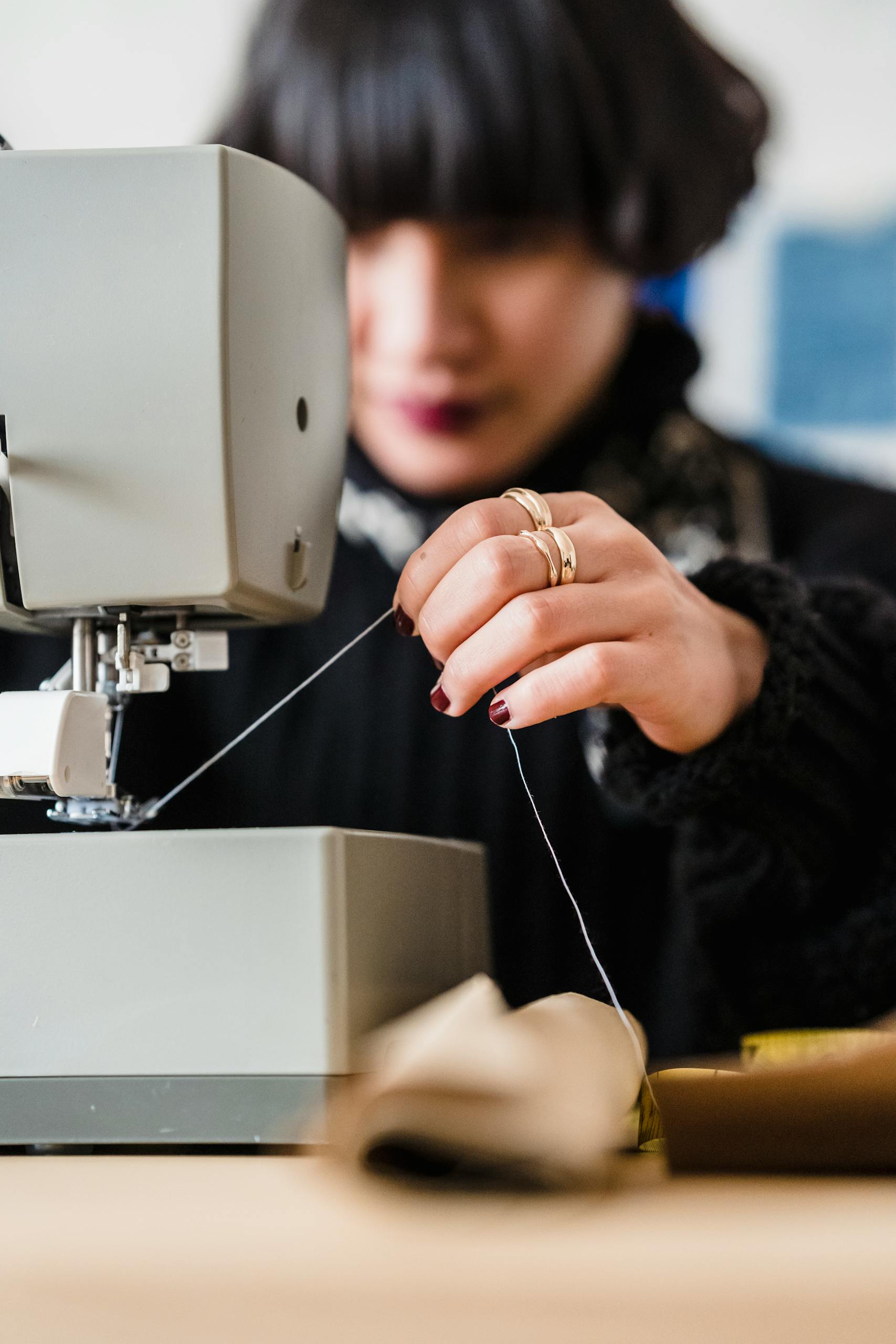 Crop concentrated young female tailor using sewing machine while working in atelier in daytime