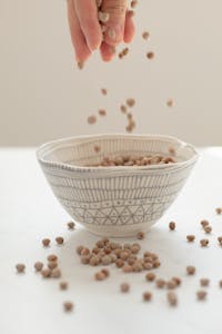 A hand pours mustard seeds into a patterned bowl, capturing the motion with elegance.