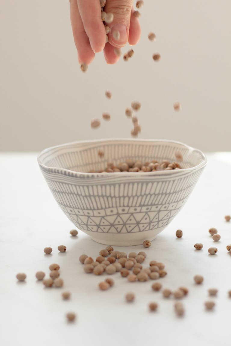 A hand pours mustard seeds into a patterned bowl, capturing the motion with elegance.